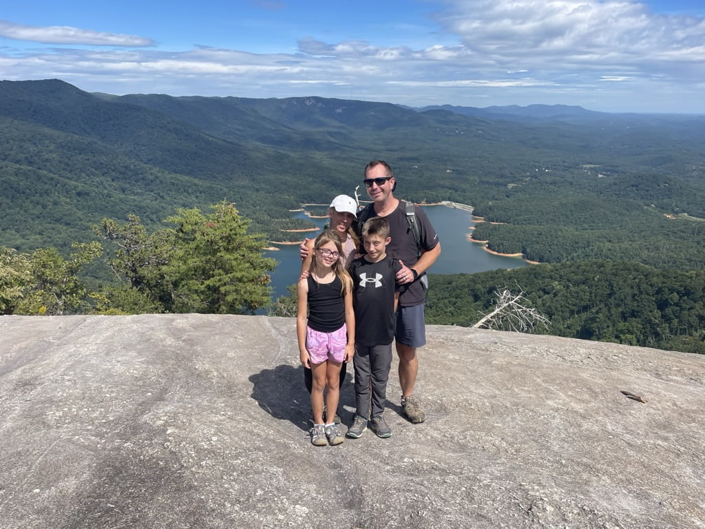 A family standing on top of a mountain overlooking a lake.