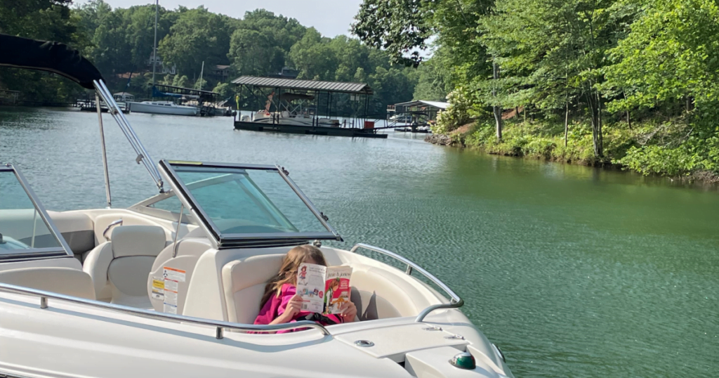 A little girl sitting in the back of a boat reading a book.