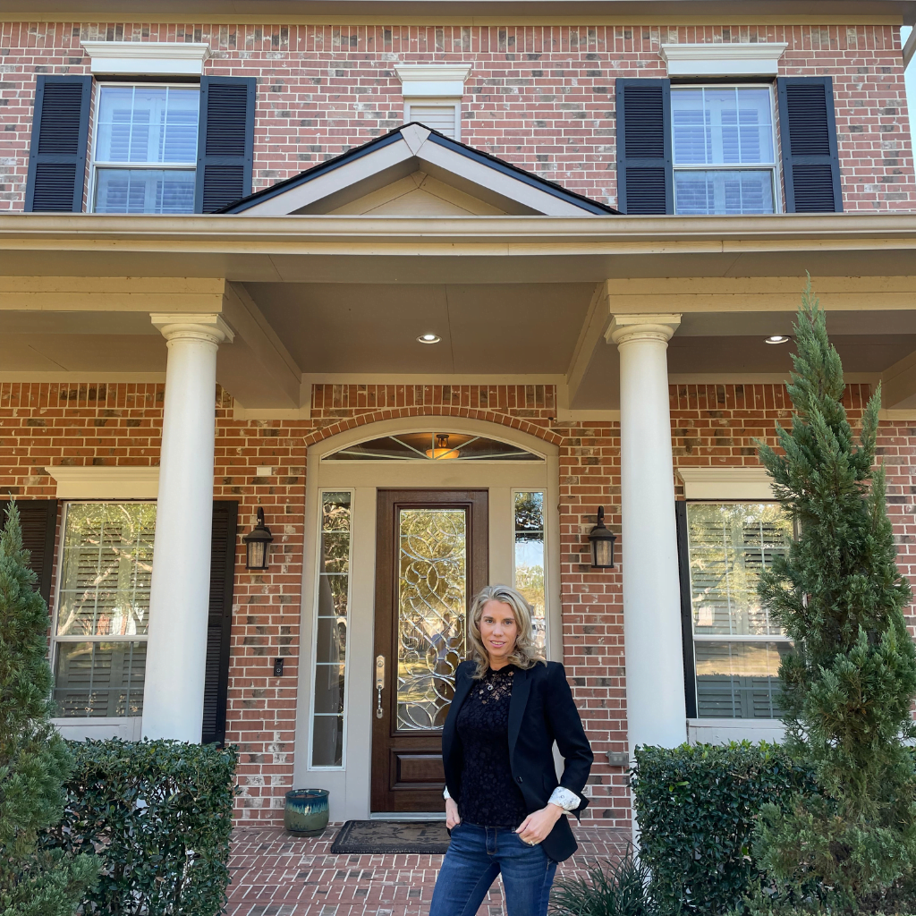 A woman standing in front of a brick house.
