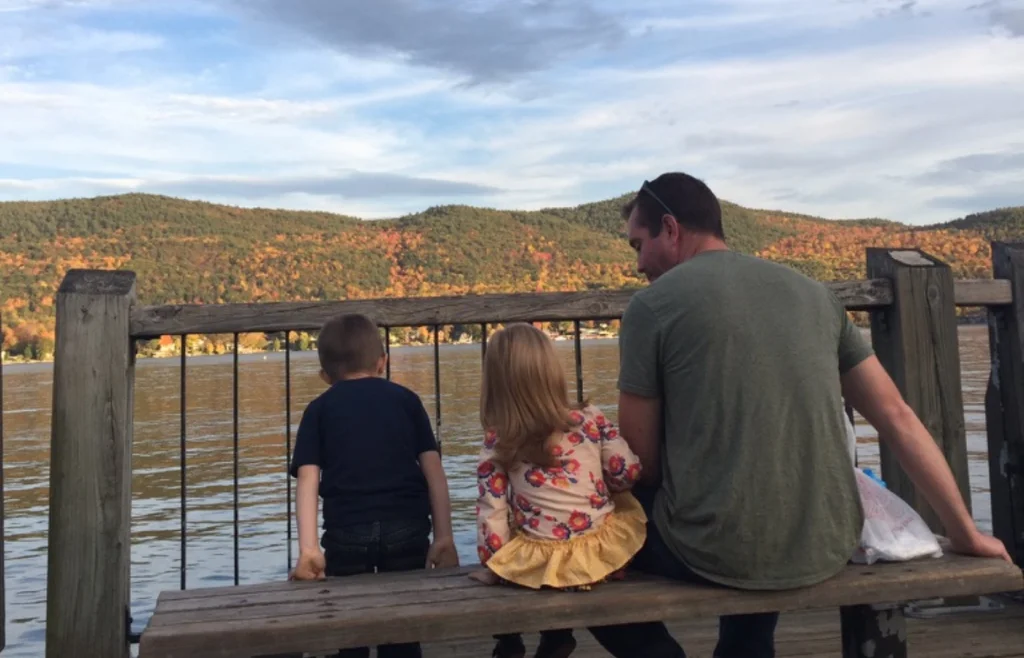 A man and two children sitting on a bench overlooking a lake.